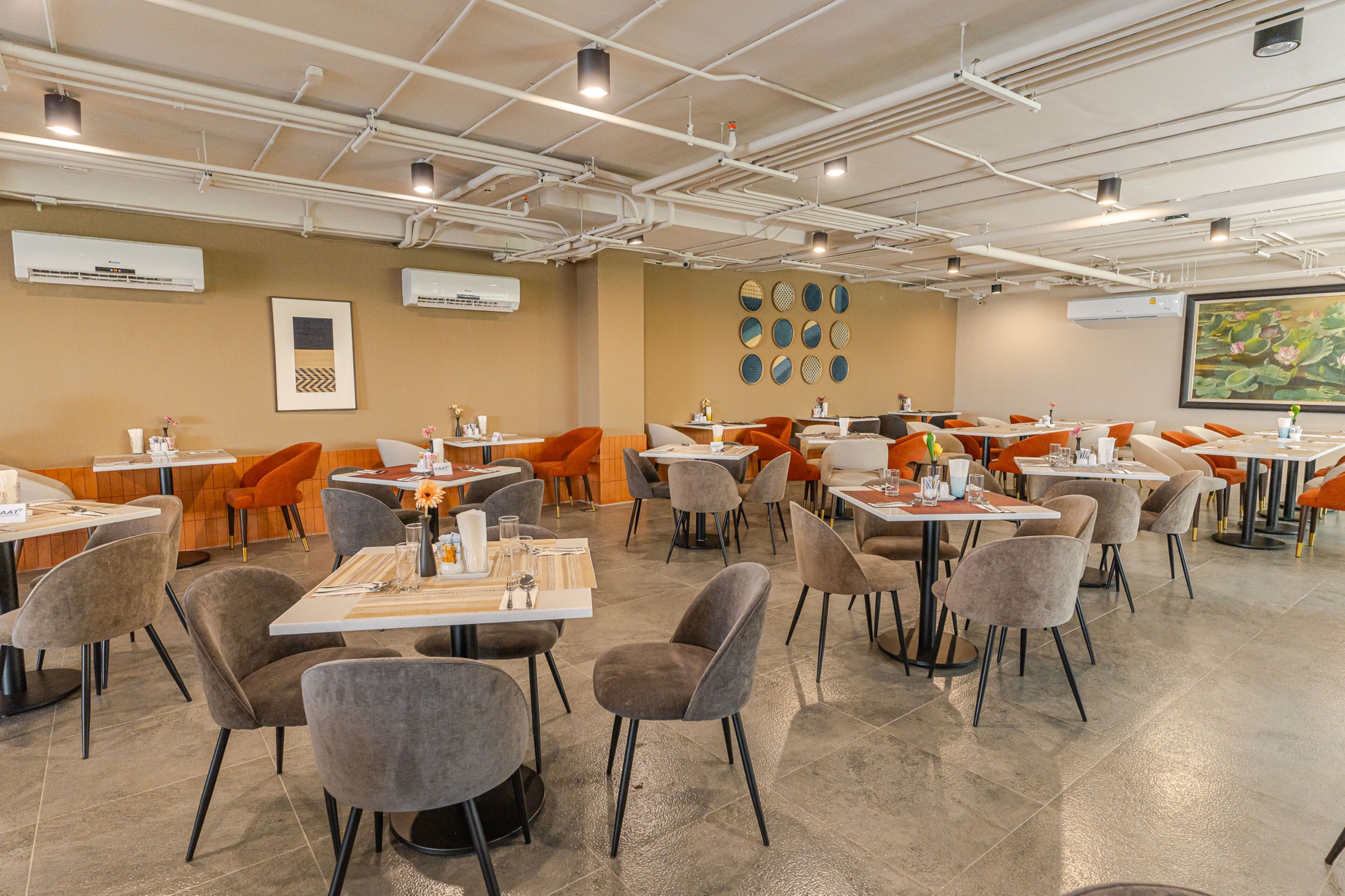 A modern dining area with multiple tables and chairs, air conditioning units, and a large painting on the wall.