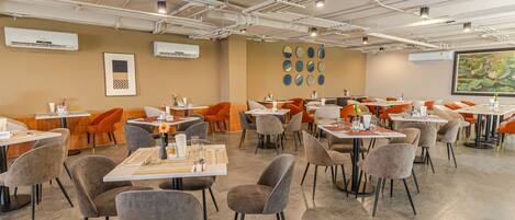 A modern dining area with multiple tables and chairs, air conditioning units, and a large painting on the wall.