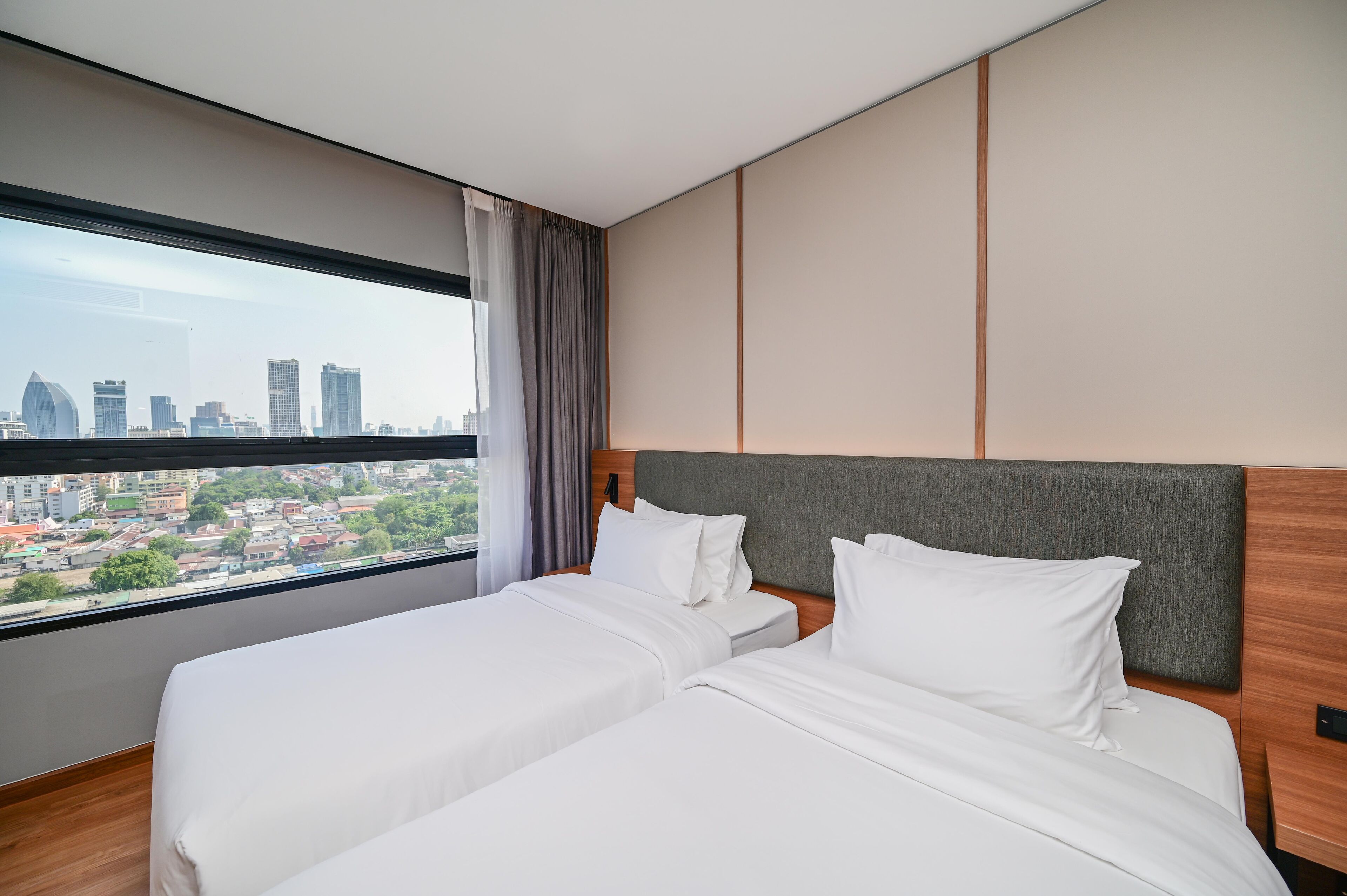 A hotel room with two beds, a large window with a city view, and a modern design.