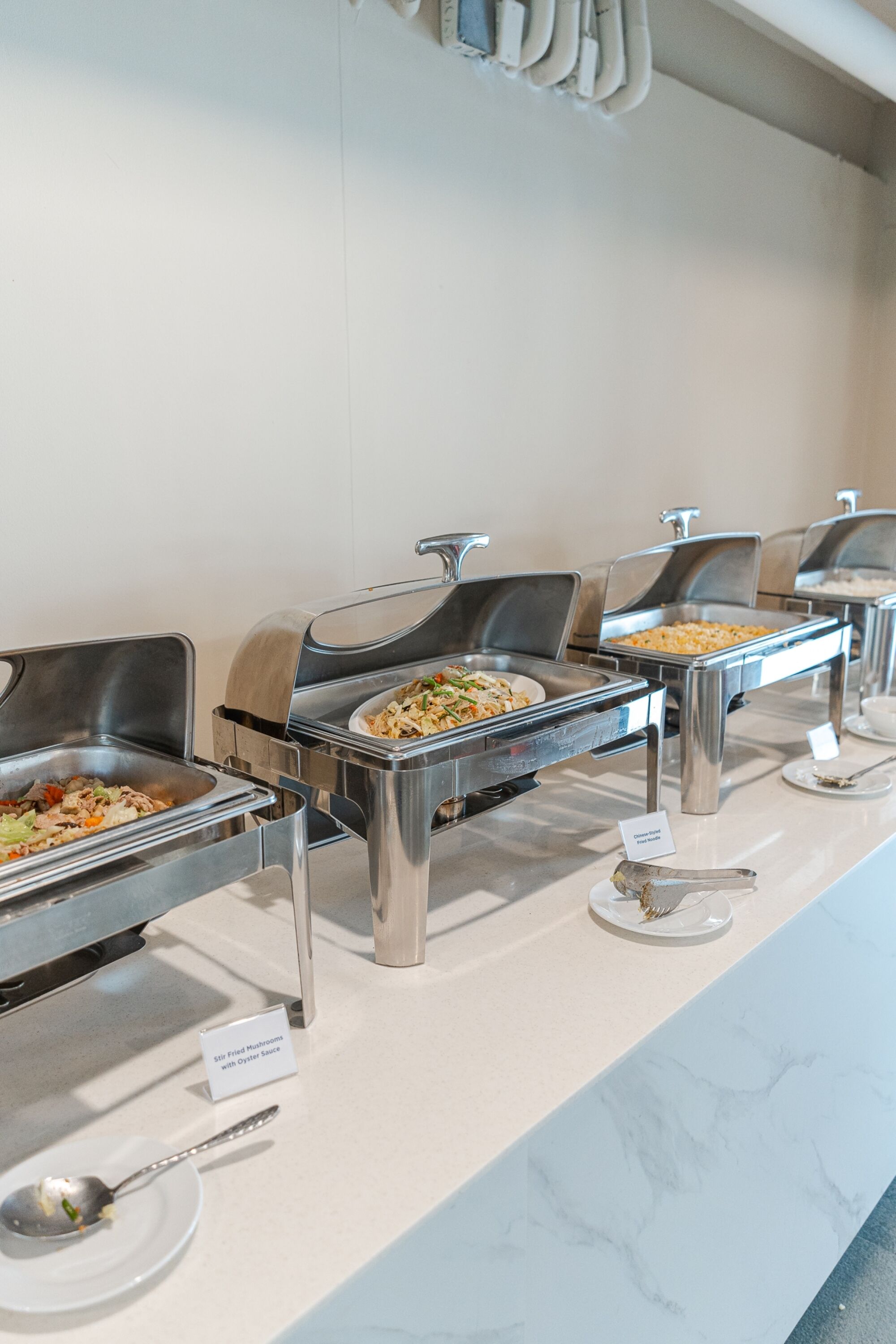 A buffet setup with multiple stainless steel serving stations, each labeled with different food options.