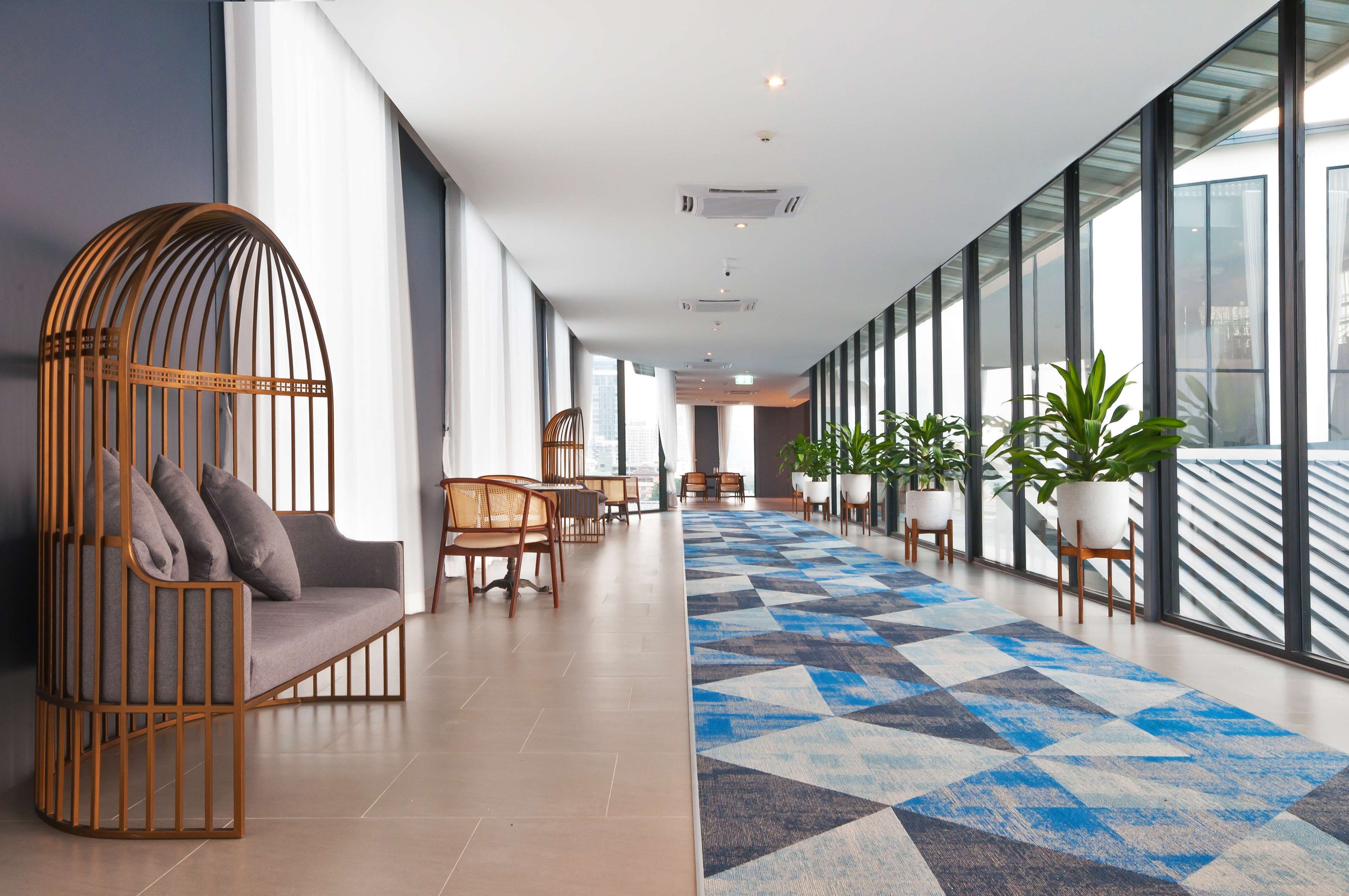 A modern hotel lobby with a long corridor, seating area, and large windows.