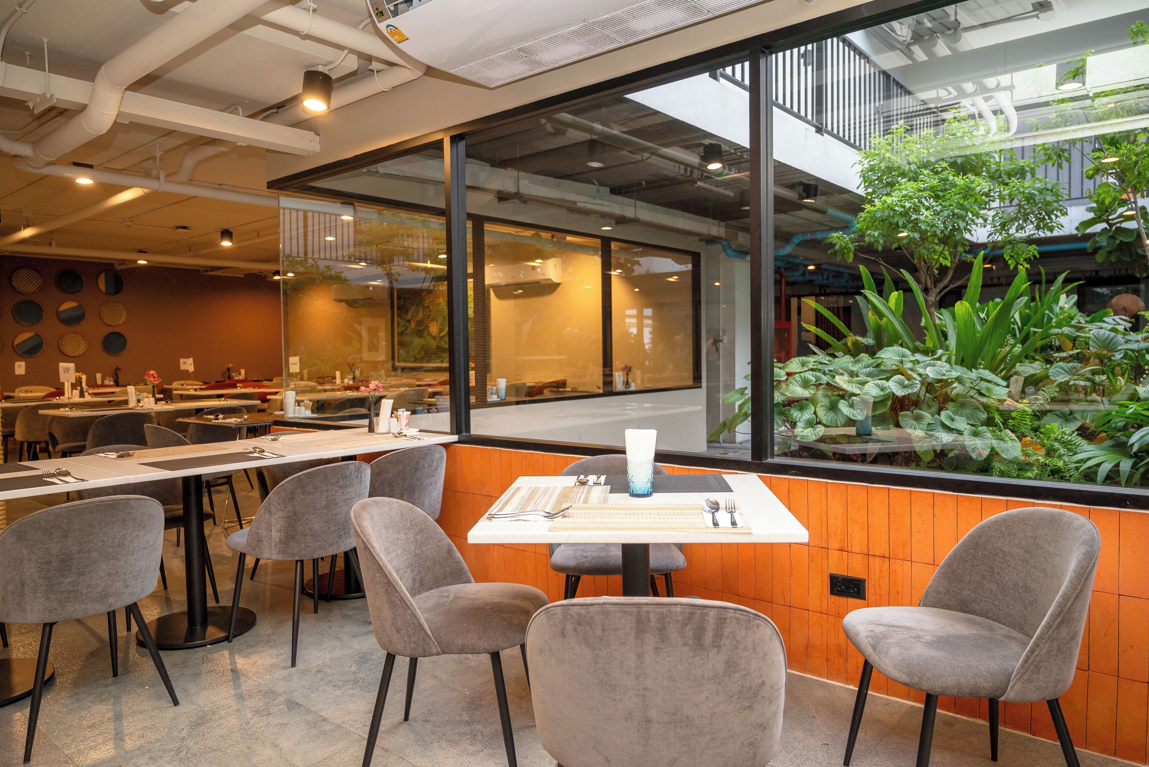 Un comedor interior con mesas y sillas, ventanas amplias y vistas a zonas verdes.