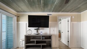 A modern living room with a flat-screen TV mounted on a wall, a grey entertainment unit, a white chair, and a sliding glass door leading to an outdoor area.
