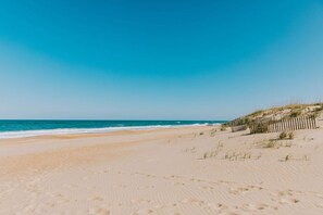 Una playa arenosa con huellas, una valla de madera y el océano al fondo.