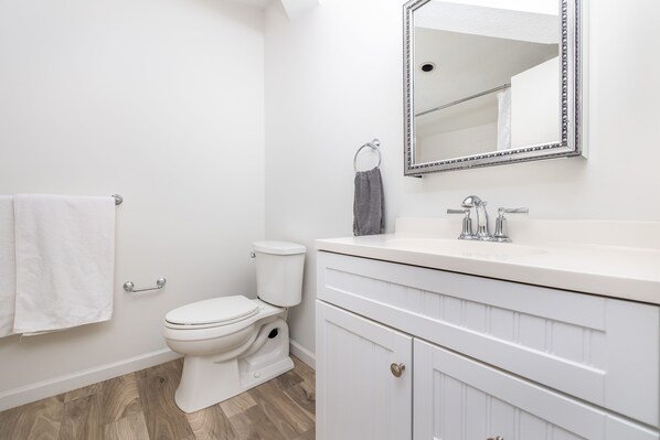 A bathroom with a white toilet, a sink with a mirror above it, and a towel rack with a white towel. - Exquisite Downtown Loft Apartment (Hartford)