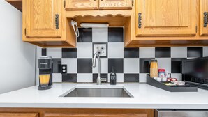 A kitchen with wooden cabinets, a black and white checkered backsplash, a coffee maker, a sink, and a microwave. - Exquisite Downtown Loft Apartment (Hartford)