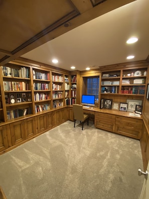 Una biblioteca con estanterías de madera, un escritorio con computadora y un ventanal.