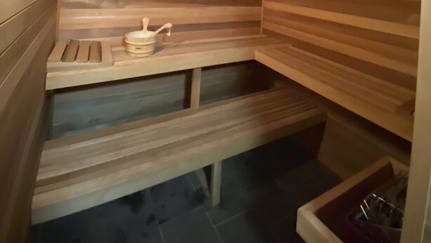 A sauna with wooden slats, a bench, a small table with a bucket, and a light fixture. - Luxury Home For Rent NBA All Star Weekend (Salt Lake City)