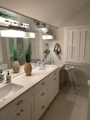 A modern bathroom with a large mirror, two sinks, a vanity, and a stool.