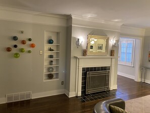 Una sala de estar con chimenea, repisa blanca y estante de pared con adornos.