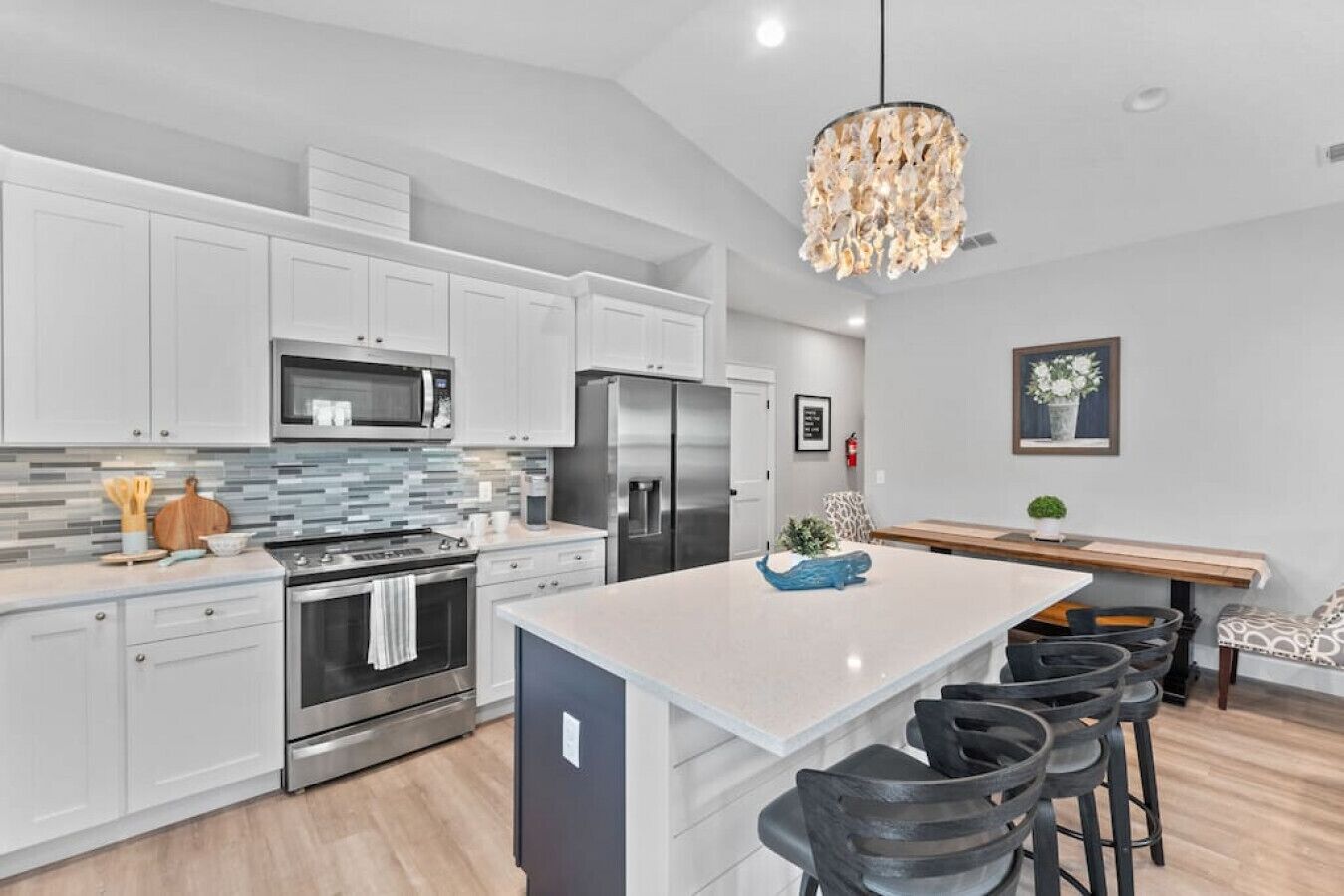 A modern kitchen with white cabinets, stainless steel appliances, a central island with bar stools, and a decorative chandelier.