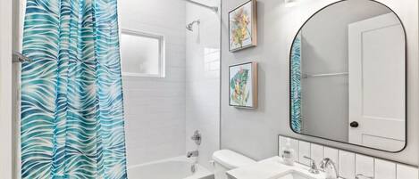A bathroom with a shower, toilet, sink, and a large mirror.