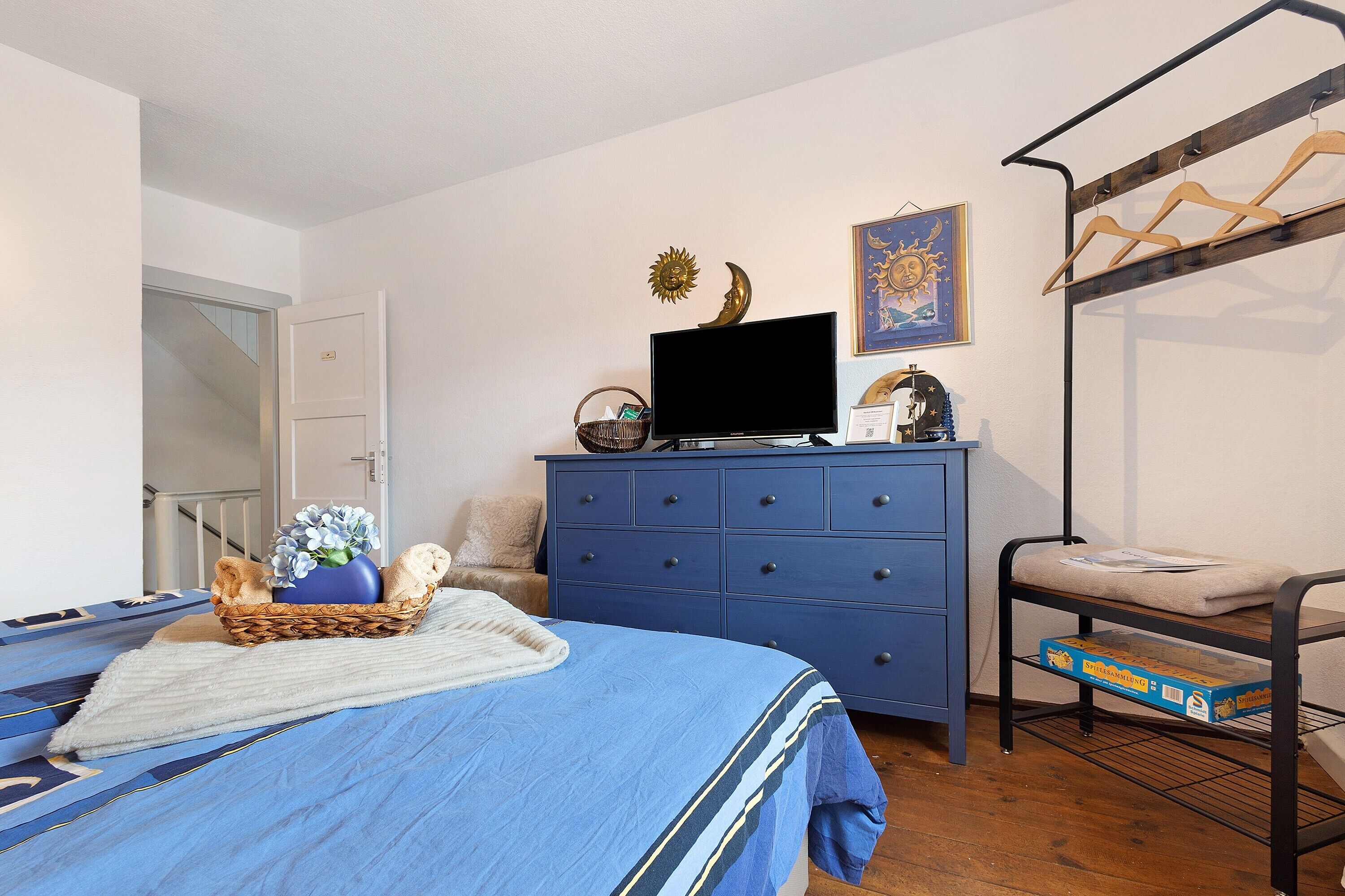 A bedroom with a bed, a dresser, a TV, a bunk bed, and a wall with a sun and moon decoration.