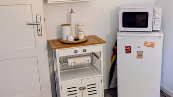 Een compacte kitchenette met een magnetron, een klein kastje met glazen deuren en een houten plank met keukengerei.