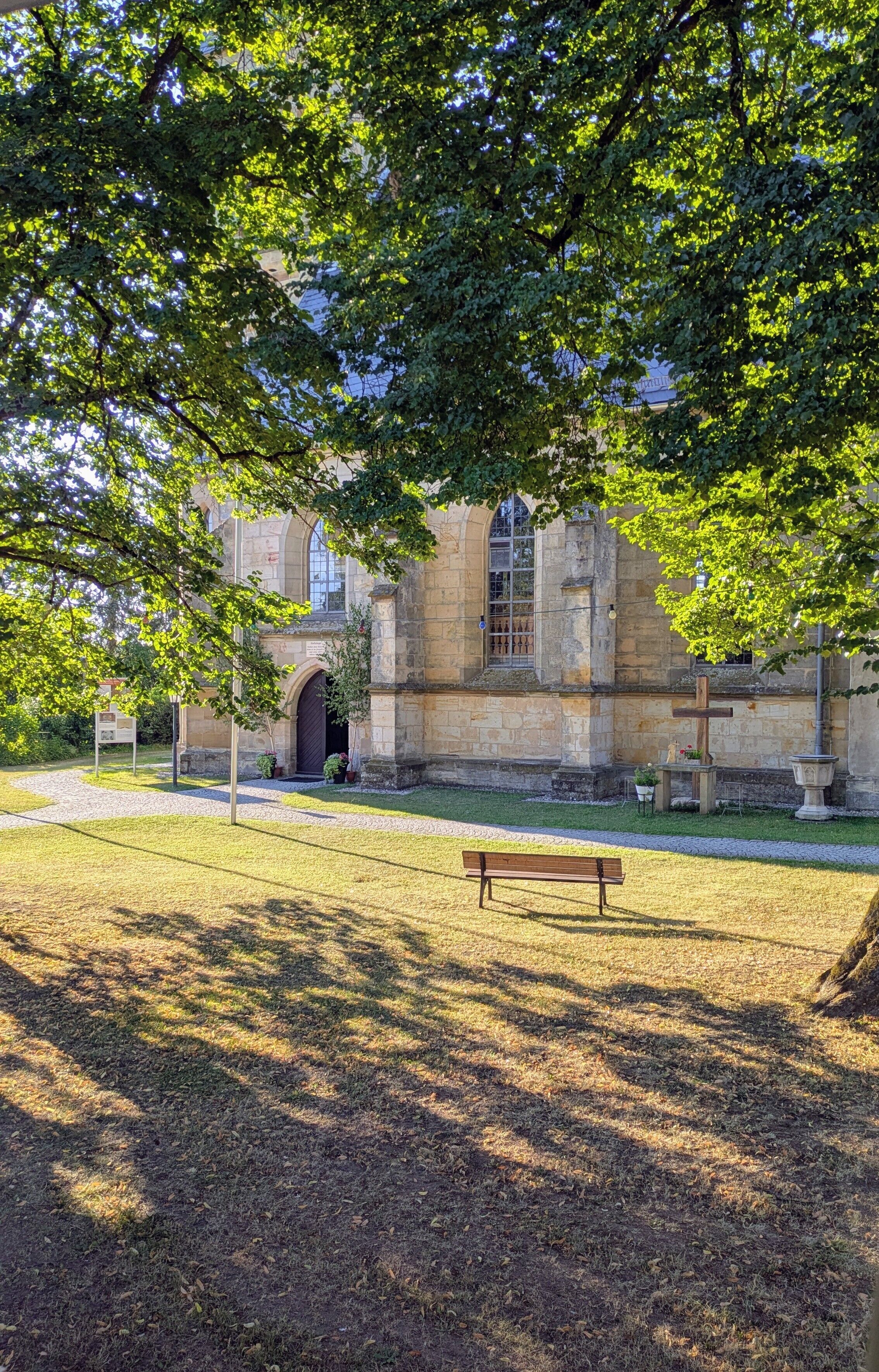 A stone building with a large arched entrance, a bench, and a grassy area.