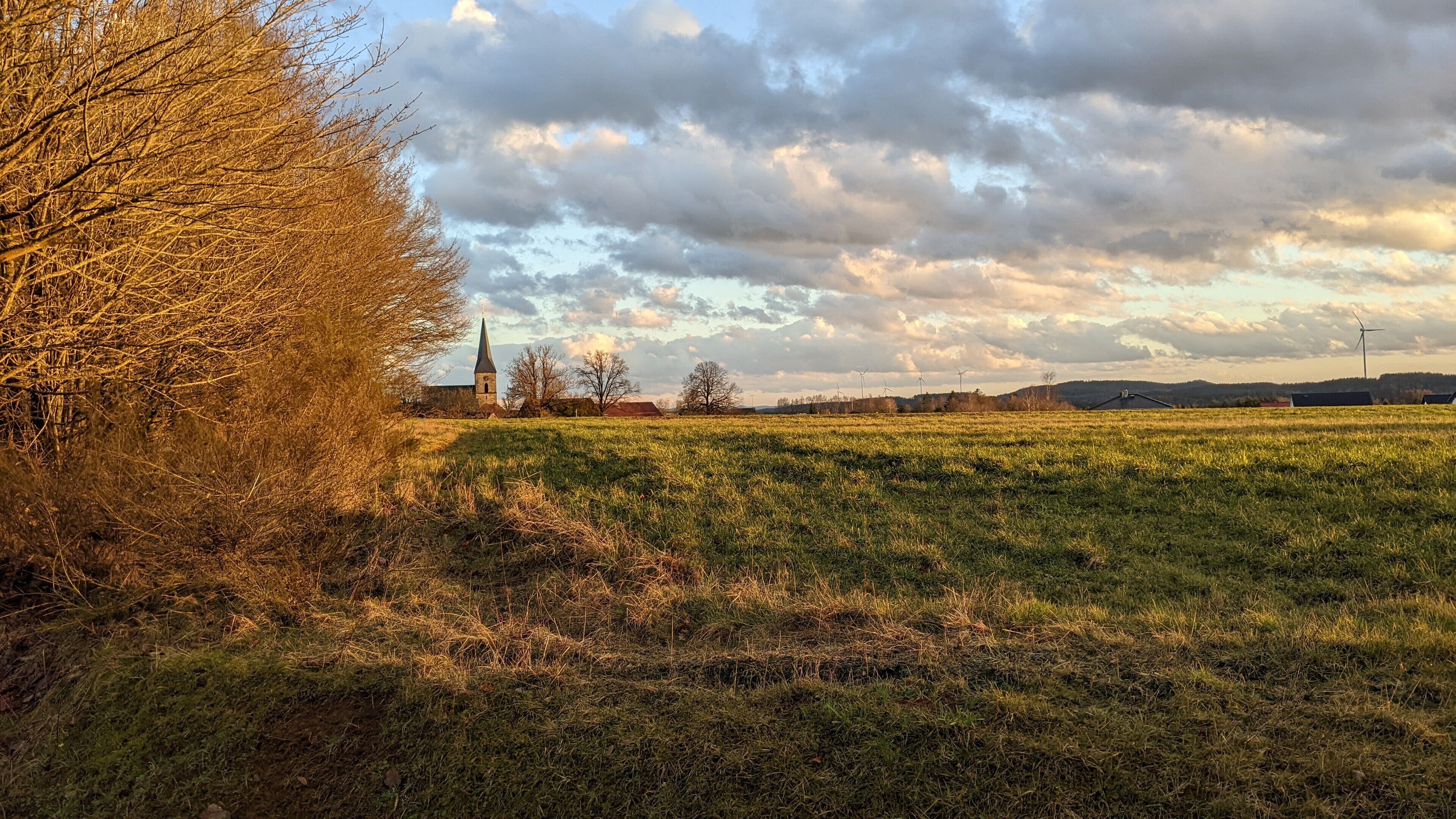 A rural landscape with a church, wind turbines, and open fields.