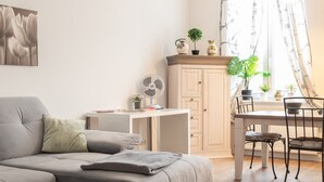 Una sala de estar moderna con un sofá gris, una mesa de comedor con sillas, una pequeña área de cocina y un ventanal con cortinas translúcidas.