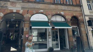 Un edificio de ladrillo con la entrada de una tienda que dice 'Sven Henkel' y una estatua decorativa de un cerdo.