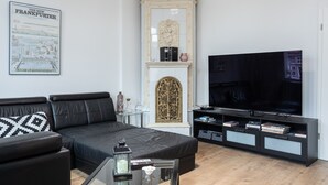 Una sala de estar moderna con un sofá de cuero negro, una mesa de centro de vidrio, un televisor de pantalla plana, una chimenea con adornos y un mapa enmarcado en la pared.