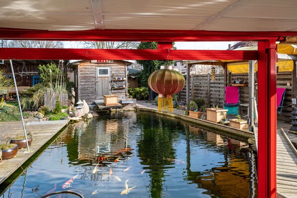 A koi pond with a wooden deck, a small shed, and a red structure.
