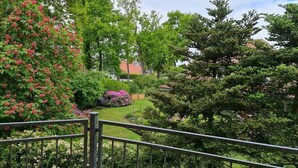 Un jardín exuberante con diversos árboles y arbustos, una barandilla de metal y un edificio al fondo.