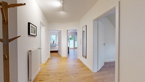 Un pasillo con suelo de madera, paredes blancas y una puerta a la derecha.