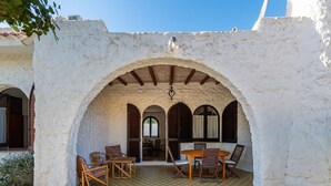 A covered outdoor seating area with a checkered floor, wooden furniture, and a view into the interior. - Palm Villa - Seaside Vacation (Muravera)