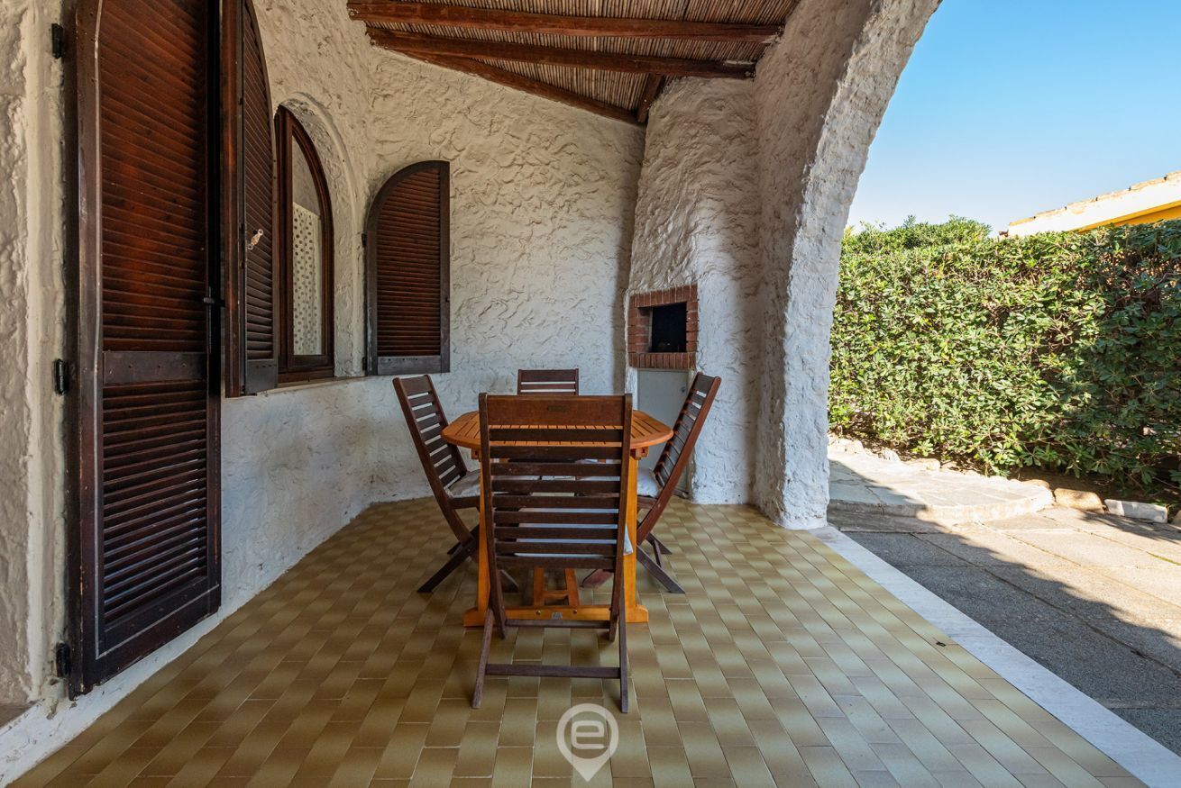 A covered patio with a checkered floor, a wooden table with chairs, and a brick fireplace.