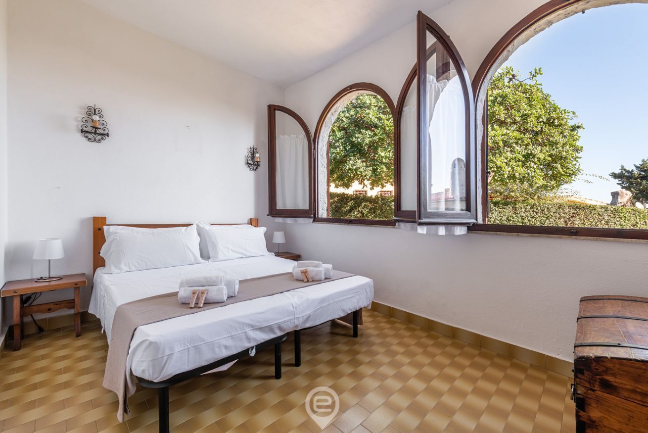 Un dormitorio con una cama grande, un banco de madera, una mesita de noche y un ventanal con vistas a la vegetación.