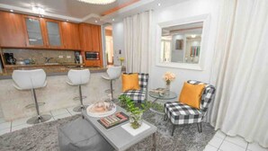 A modern living room with a kitchen area, featuring a grey sofa, a coffee table, and a checkered armchair. - Tropical Haven with private pool (Carolina)