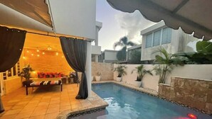 A pool area with a sunken seating area, a covered patio, and a stone wall with potted plants. - Tropical Haven with private pool (Carolina)