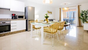 A modern kitchen with white cabinets, a stainless steel refrigerator, and a dining area with a glass table and wicker chairs. - 422 Quiet, beautiful flat with sea view, wifi (Playa Paraiso)