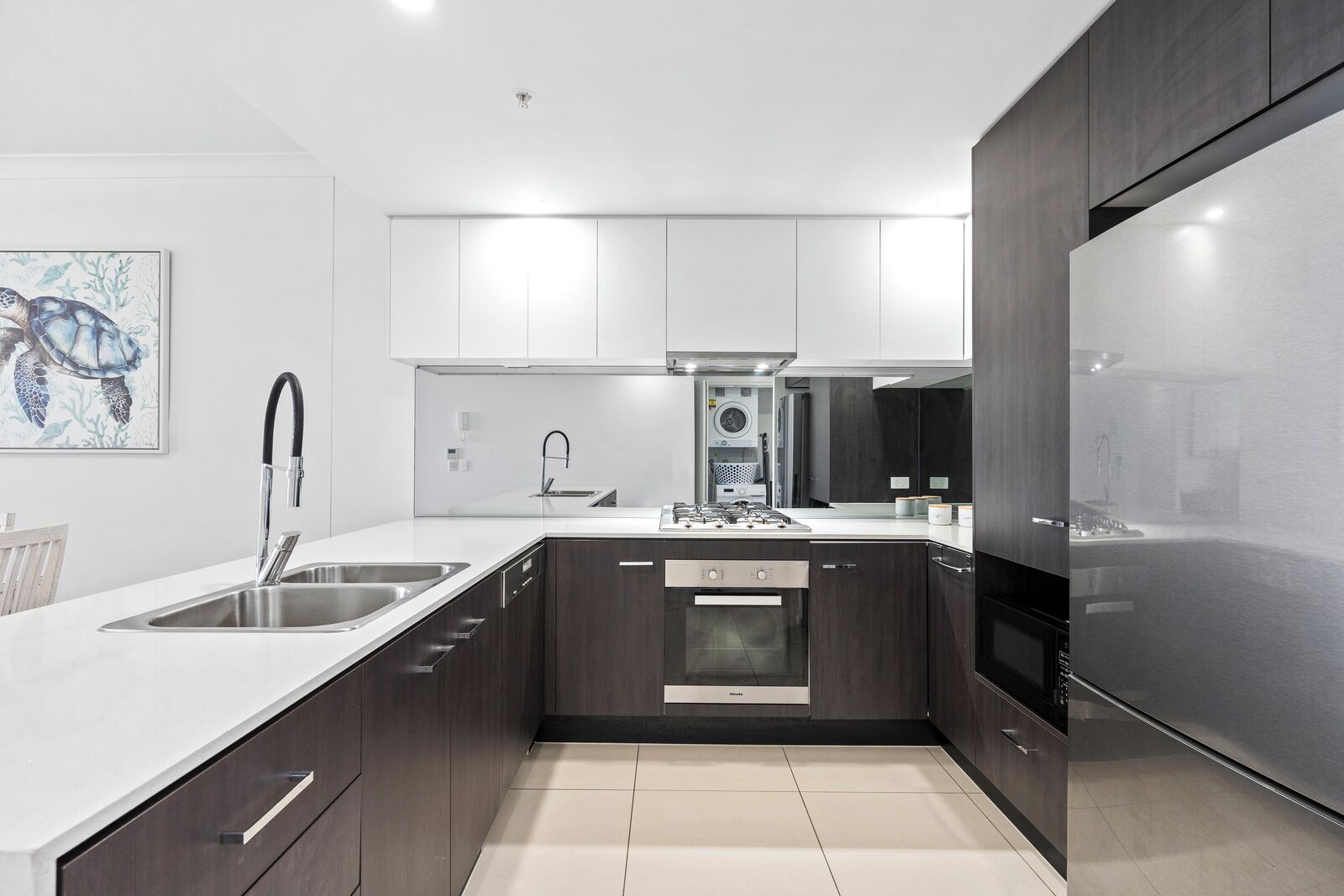 Una cocina moderna con armarios blancos, electrodomésticos de acero inoxidable y suelo de baldosas.