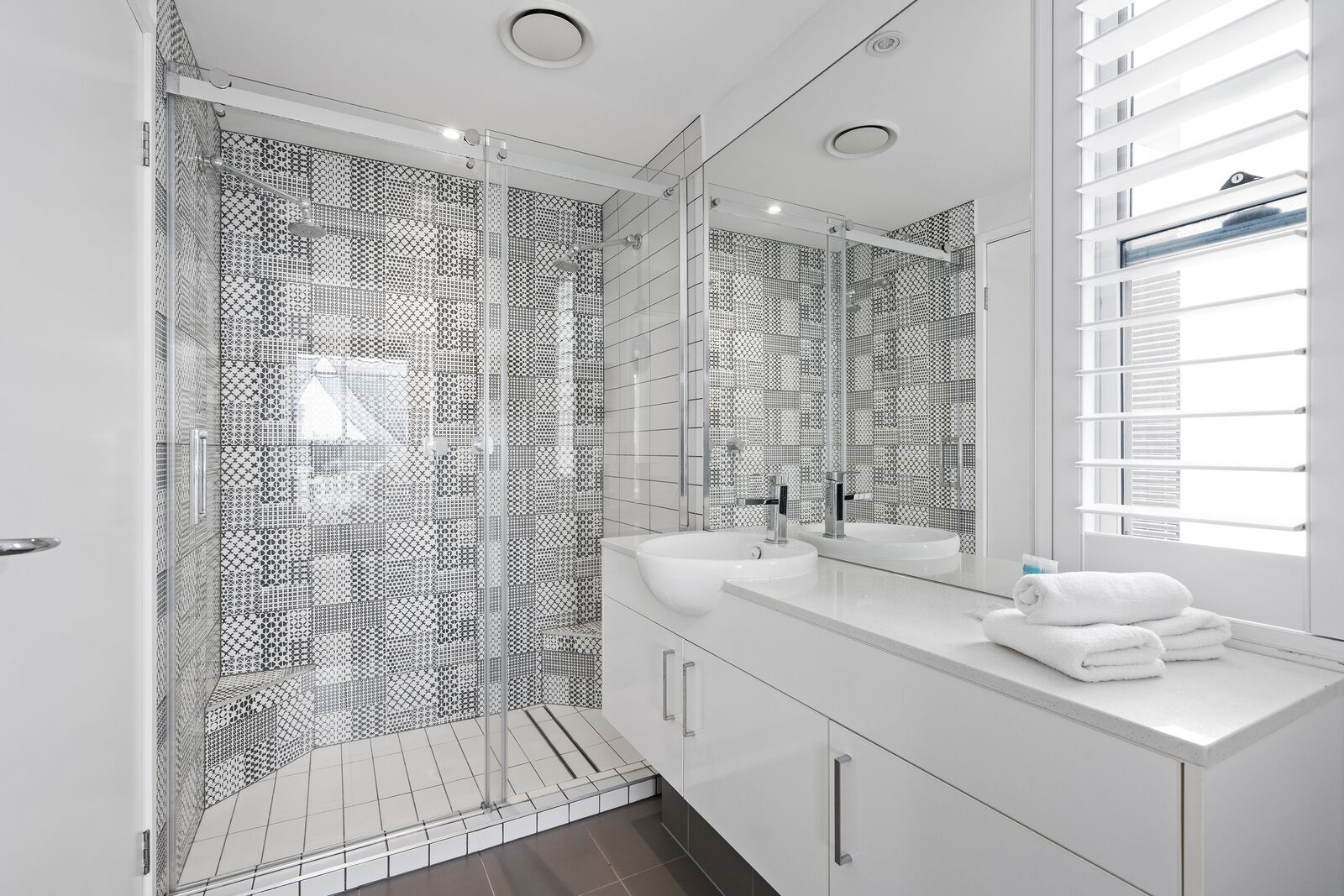 A modern bathroom with a glass-enclosed shower, white tiled walls, and a large mirror above the sink.