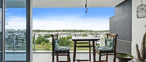 Un balcón con una mesa y dos sillas, una planta de cactus y vistas a una zona residencial.
