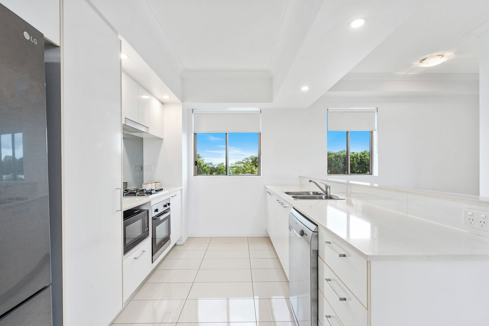 A modern kitchen with white cabinetry, stainless steel appliances, and large windows offering a view of greenery.