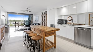 A modern kitchen with a wooden bar, white cabinets, and stainless steel appliances. - Harbour Quays Apartments (Biggera Waters)