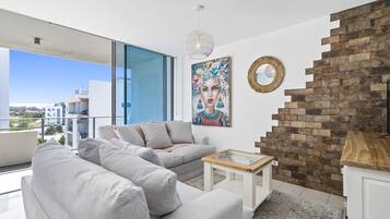 A modern living room with a grey sofa, a small table, and a staircase with a brick wall.