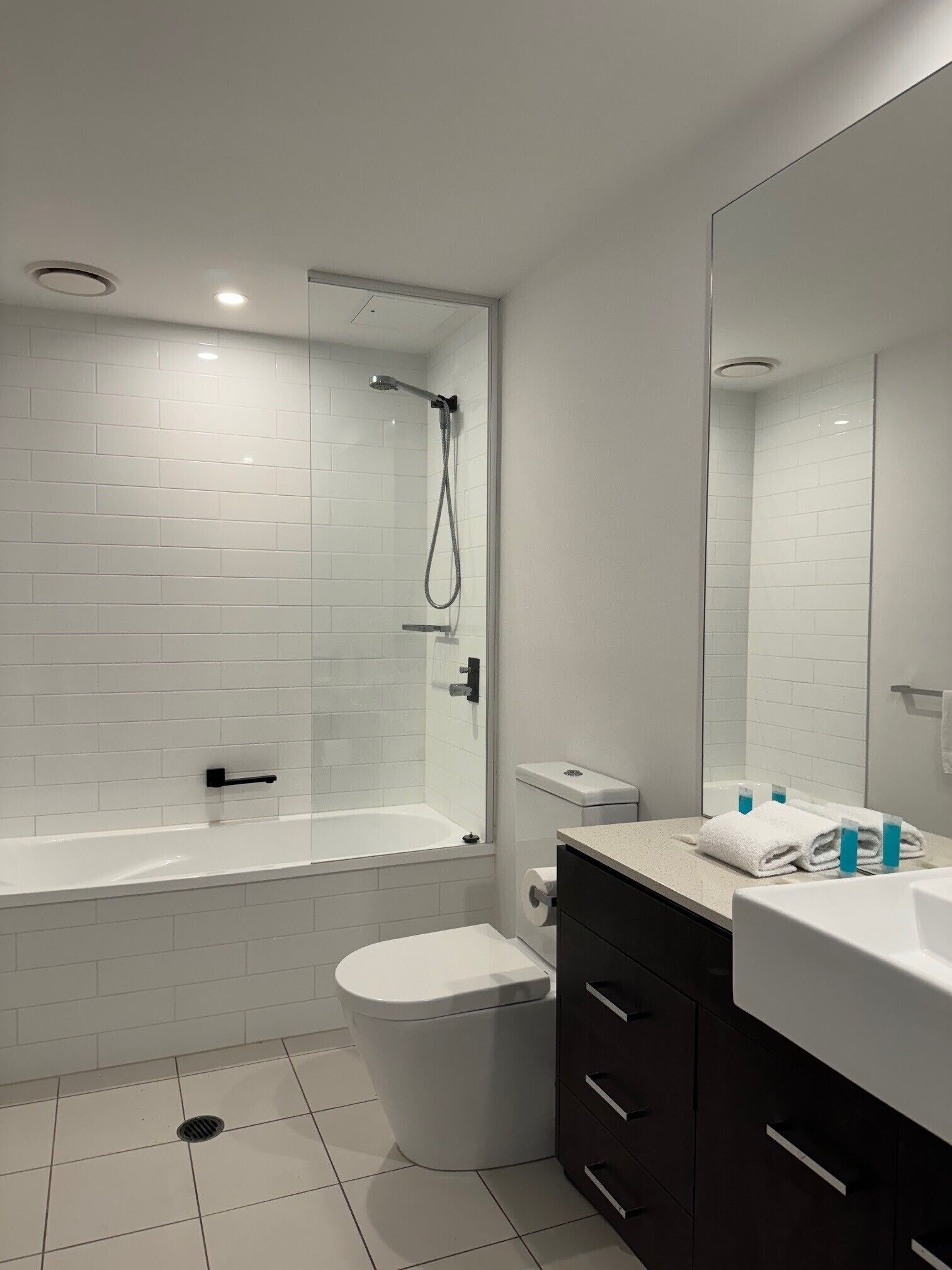 Un bagno moderno con doccia vetrata, WC bianco, lavabo con specchio e mobili scuri.