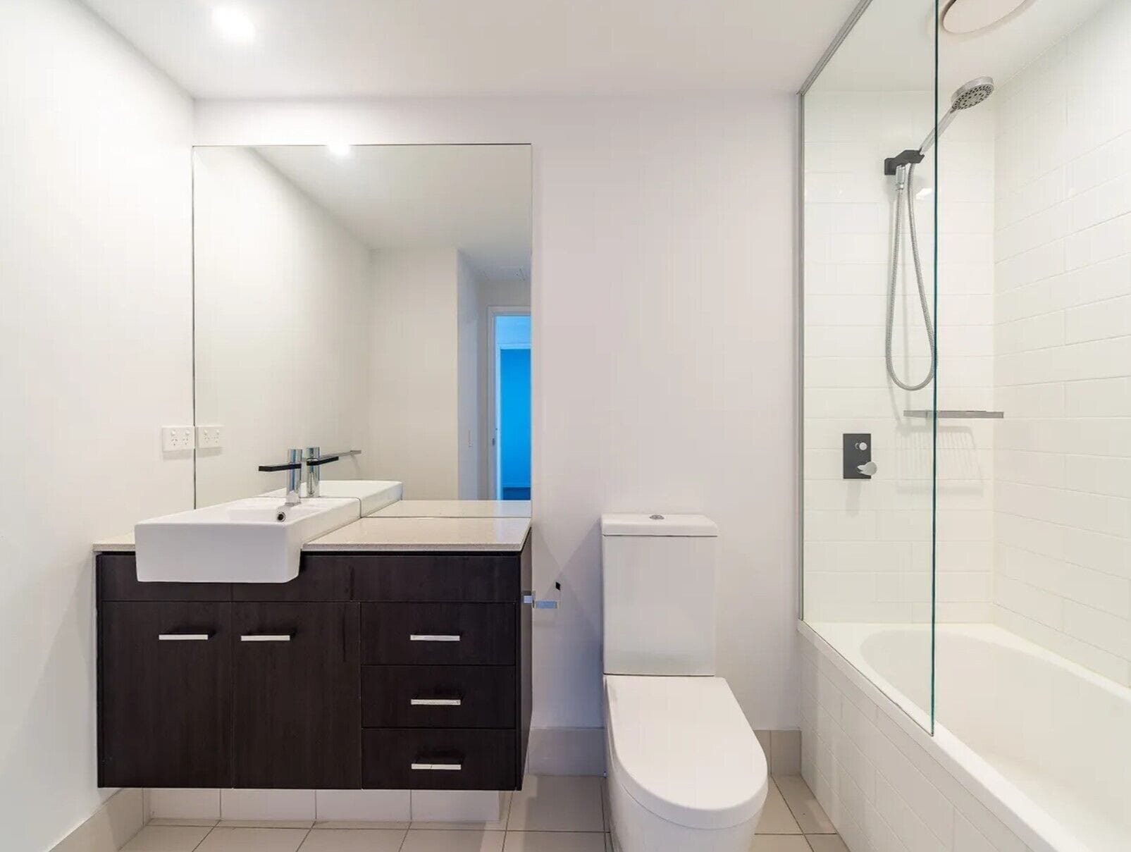 A modern bathroom with a dark wooden vanity, white sink, and toilet, and a glass-enclosed shower area.