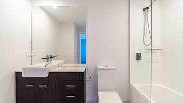 A modern bathroom with a dark wooden vanity, white sink, and toilet, and a glass-enclosed shower area.