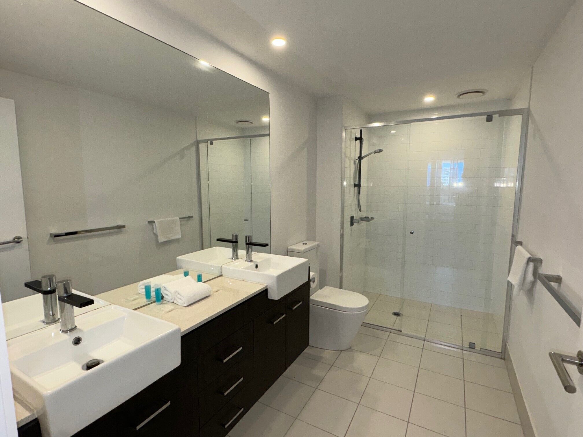 A modern bathroom with two sinks, a toilet, and a glass-enclosed shower.