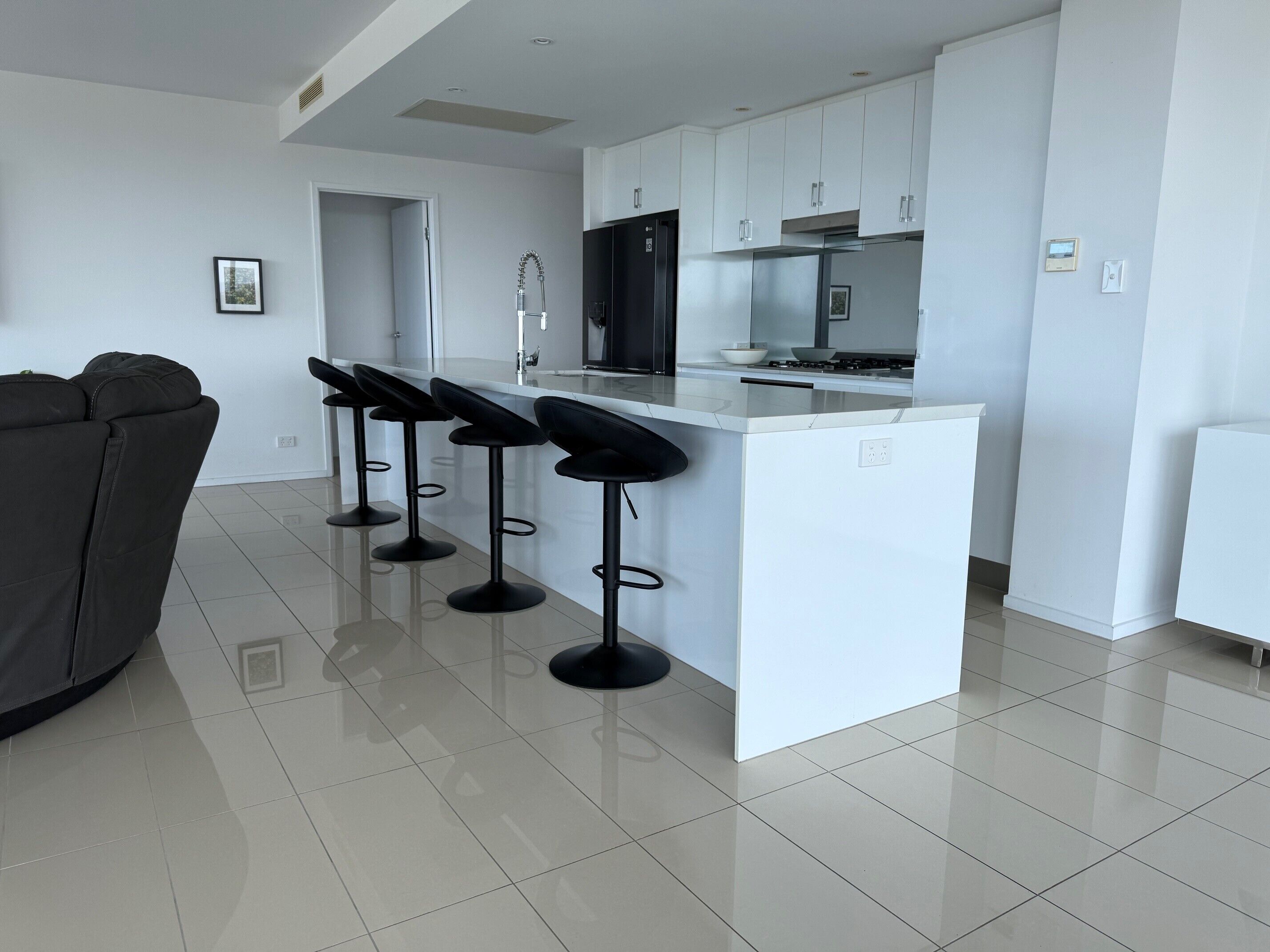 Een moderne keuken met een centraal eiland, barstoelen en een zithoek met een bank.