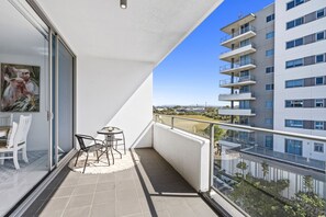 Un balcón con una mesa, sillas, un cuadro y vistas a un edificio y un paisaje.