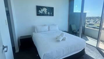 Una habitación de hotel moderna con una cama grande, un cuadro y un balcón con vista a la ciudad.