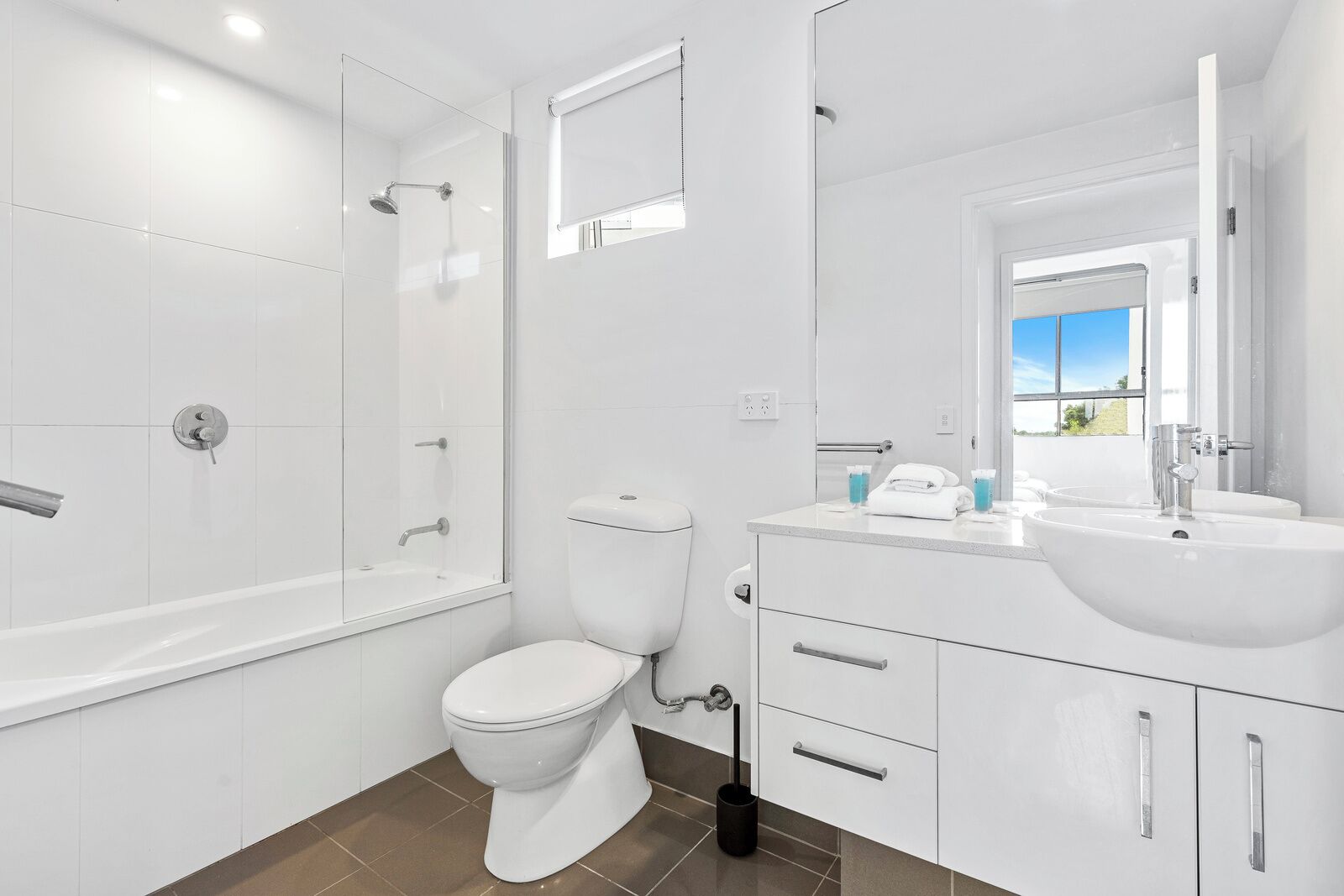 A modern bathroom with a glass-enclosed shower, a toilet, a sink with a mirror, and a window providing a view.