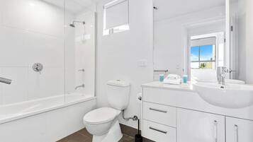 A modern bathroom with a glass-enclosed shower, a toilet, a sink with a mirror, and a window providing a view.