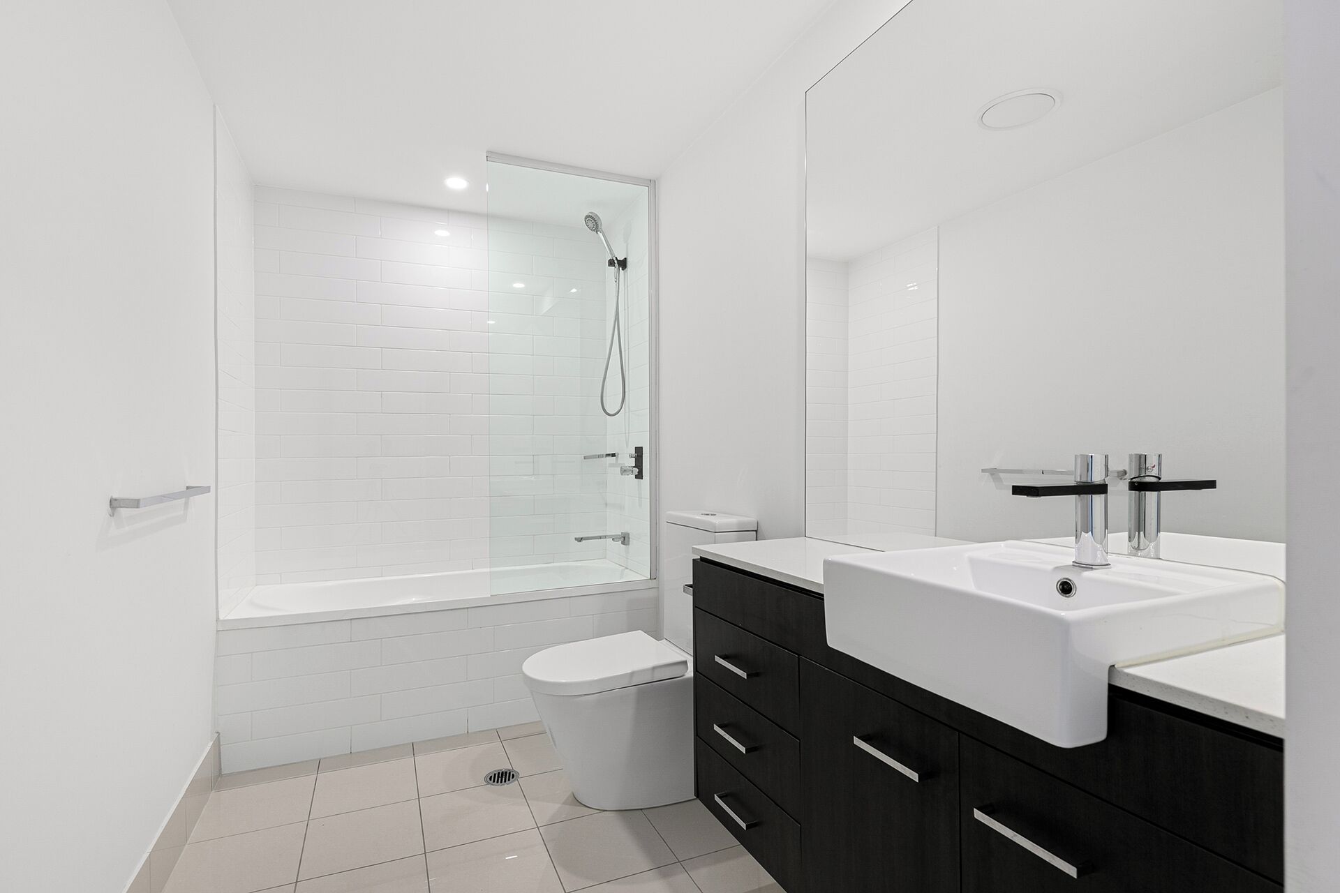Un baño moderno con ducha de vidrio, inodoro blanco y tocador con lavamanos y espejo.