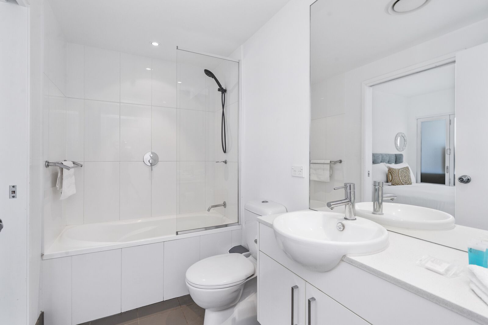 A modern bathroom with a glass-enclosed shower, a white toilet, and a vanity with a sink and mirror.