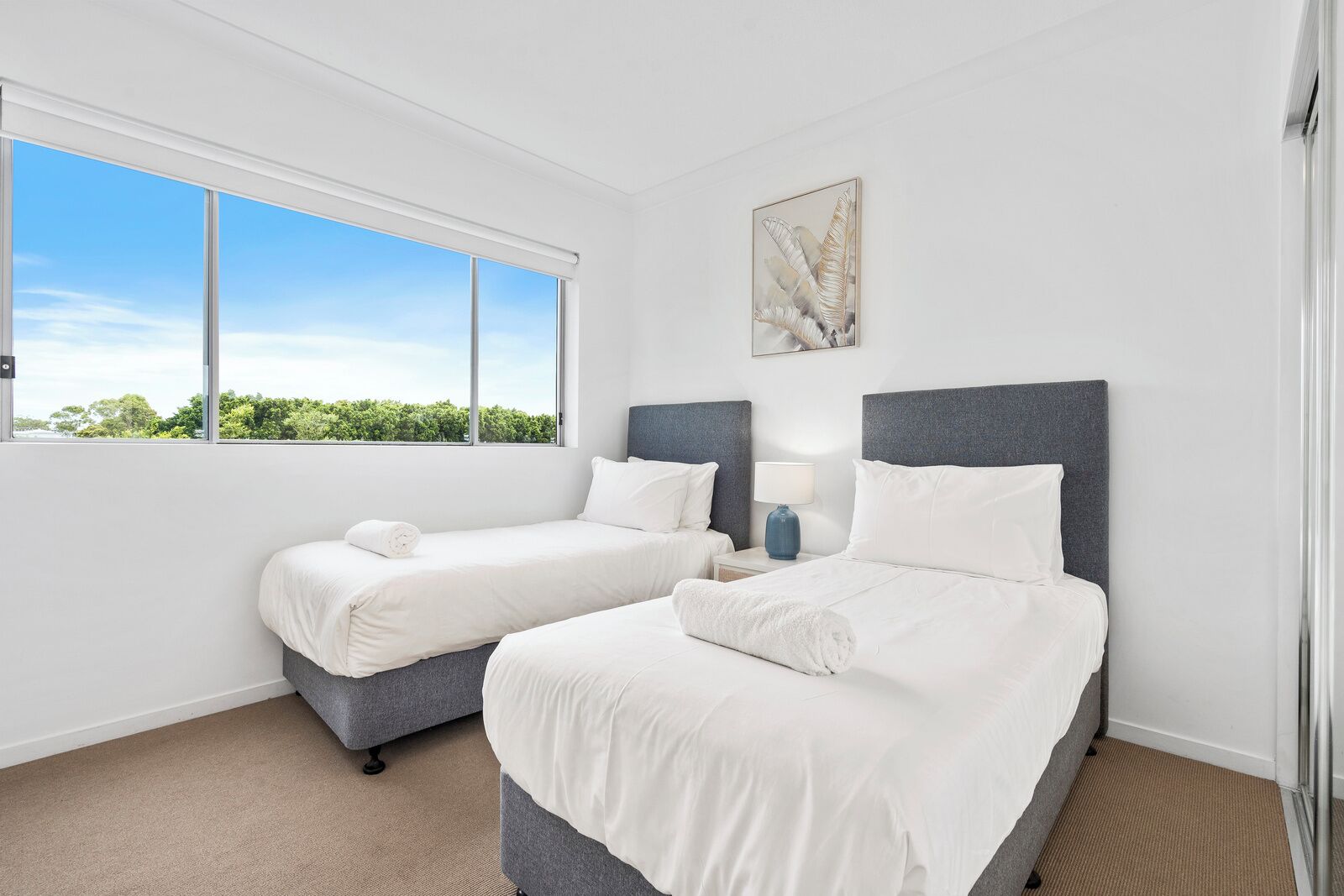 Une chambre d’hôtel avec deux lits, une grande fenêtre donnant sur un paysage verdoyant et un tableau accroché au mur.